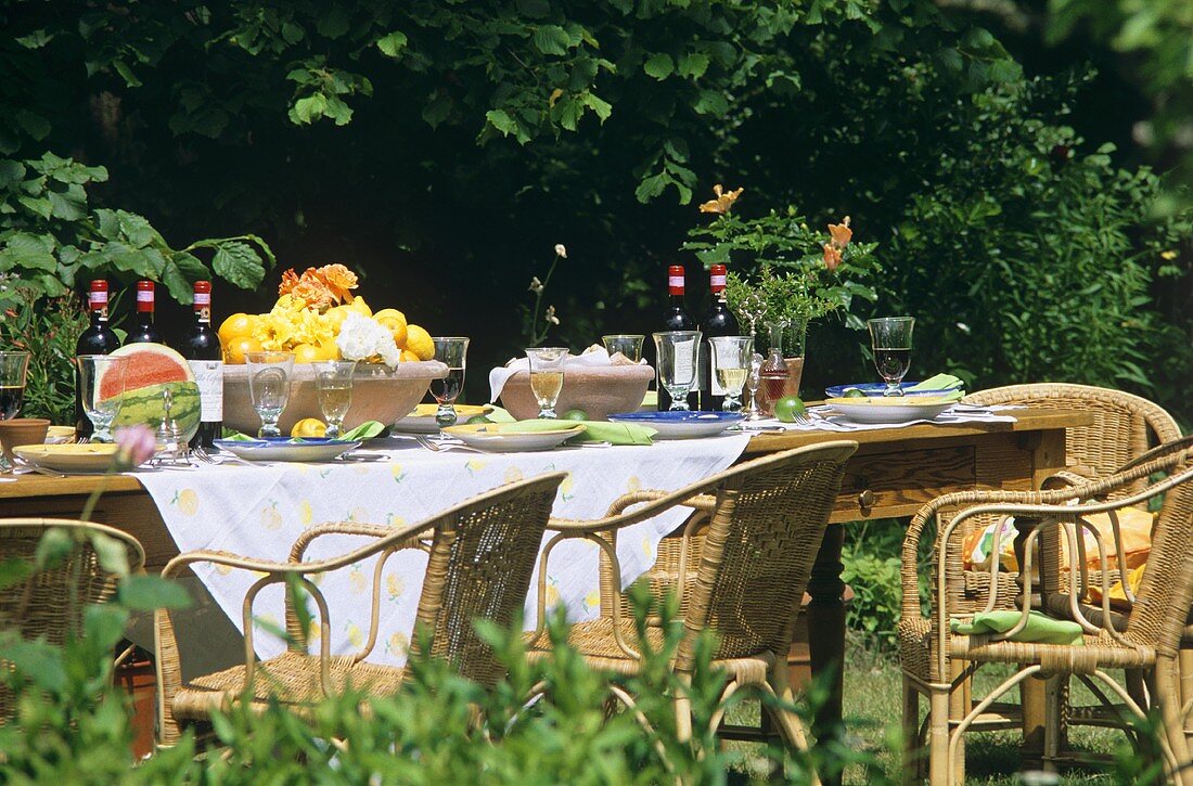 Gedeckter Tisch mit Wein und Obst im Garten mit Korbstühlen
