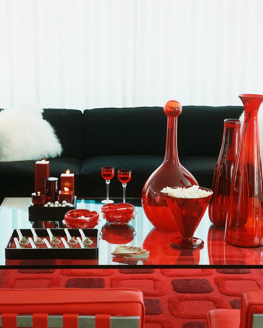 Sitzecke in Rot-Schwarz - Glastisch mit Partyhäppchen auf Löffeln, Glasvasen und Kerzen vor einem Sofa