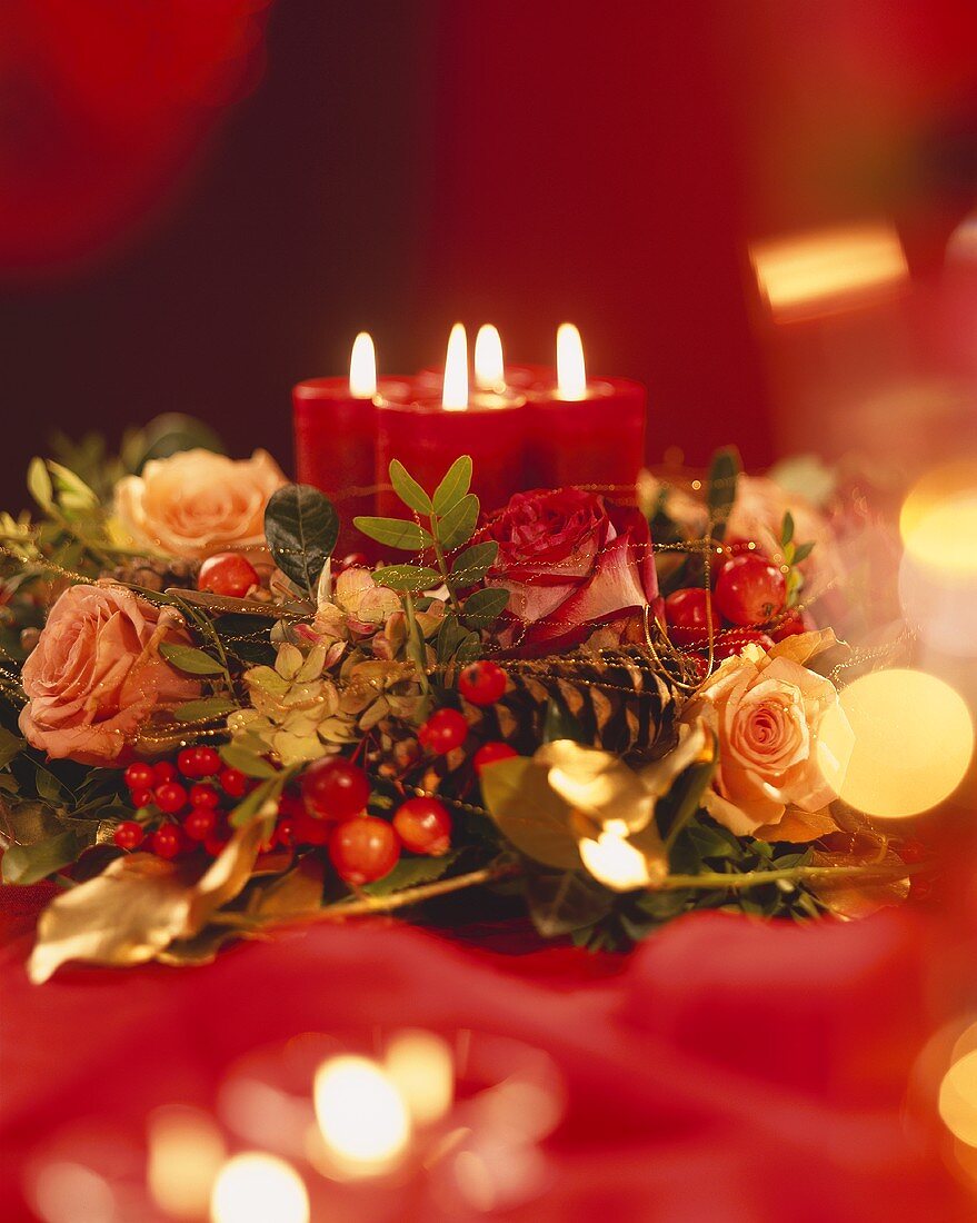 Adventsgesteck mit Rosen, Goldfäden und brennenden Kerzen