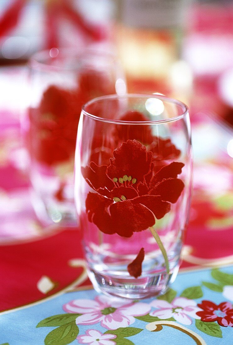 Glas mit Blumenmotiv auf bunter Tischdecke