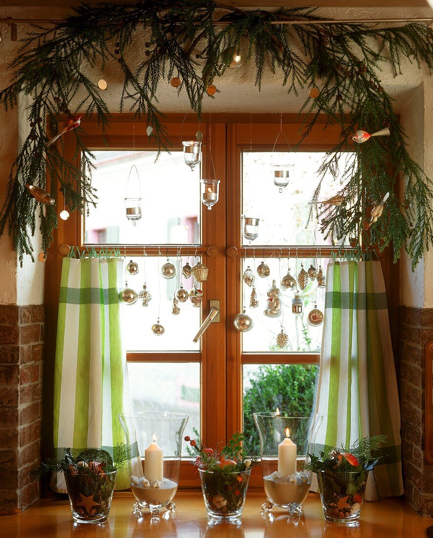 Kerzen und Tannenzweige in weihnachtlich geschmücktem Fenster