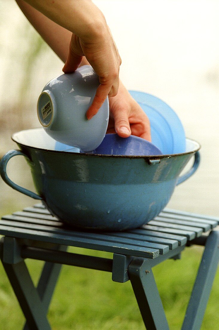 Geschirr abwaschen in blauer Schüssel auf Campinghocker