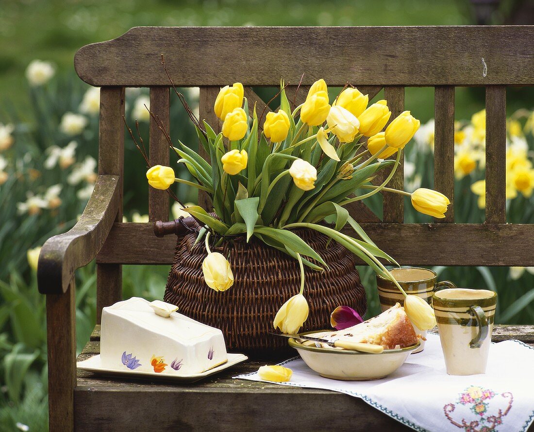 Kuchenstück, Butterdose & gelber Tulpenstrauss auf Gartenbank