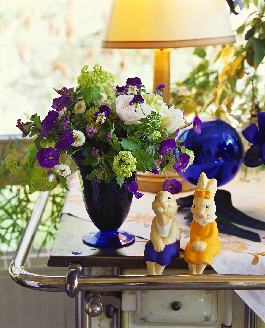 Zwei Osterhasenfiguren und Blumenstrauss auf Küchenherd