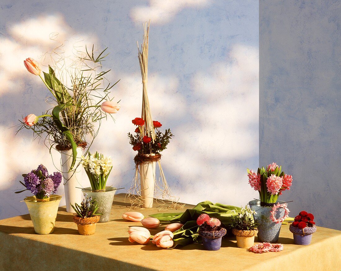Tisch mit verschiedenen Frühlingsblumen in Töpfchen und Vasen