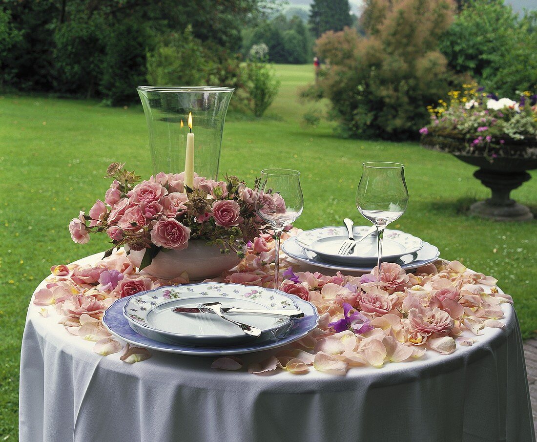 Romantic table with rose petals, arrangement of roses in garden