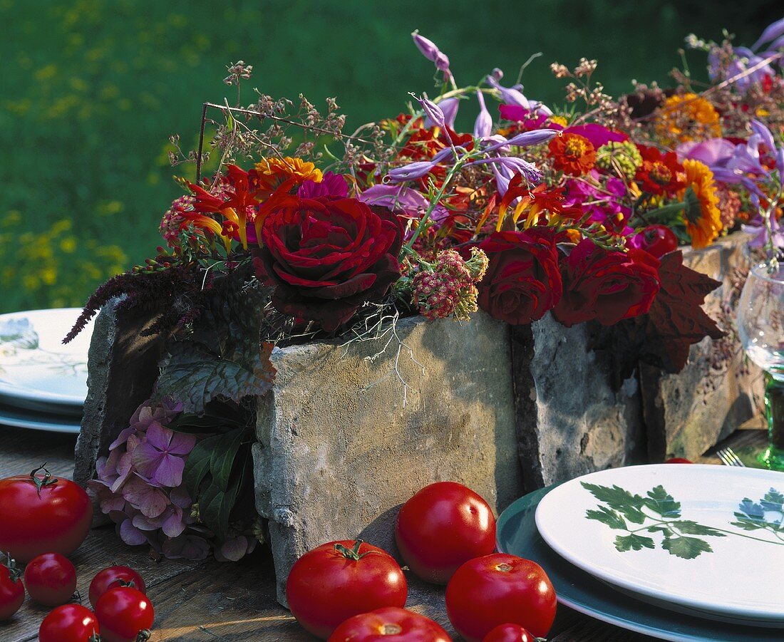 Blumenarrangement in kräftigen Farben umgeben von Tomaten