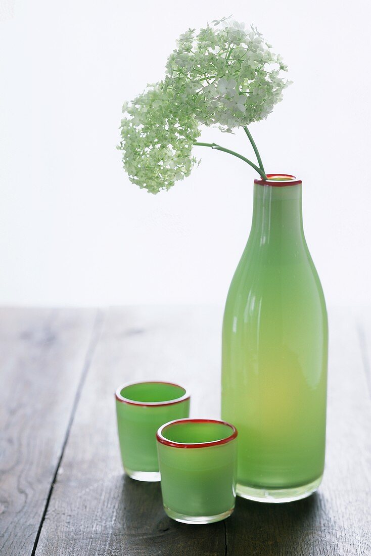 Grüne Flasche mit Blumen und grünen Gläsern