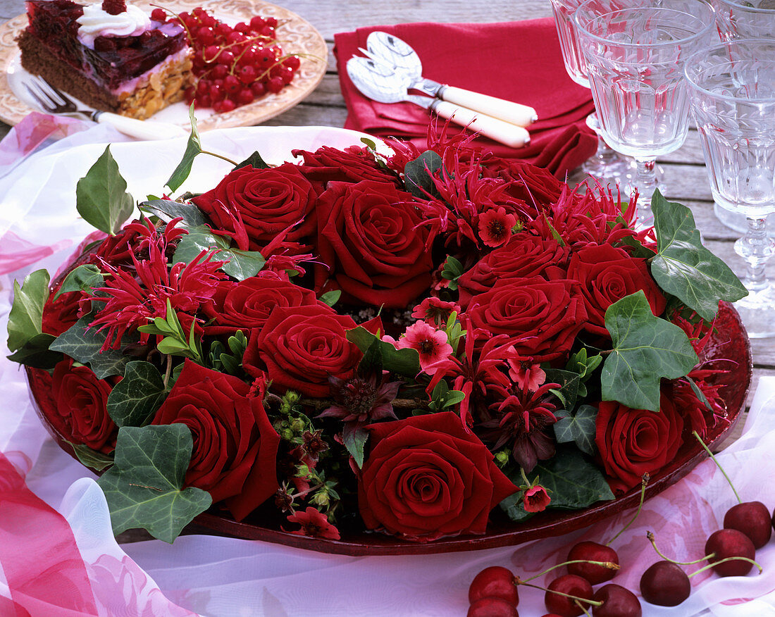 Romantic table decoration of red roses, Monarda & ivy on plate