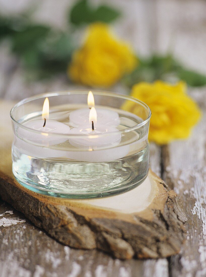 Drei schwimmende Kerzen auf einer Holzplatte