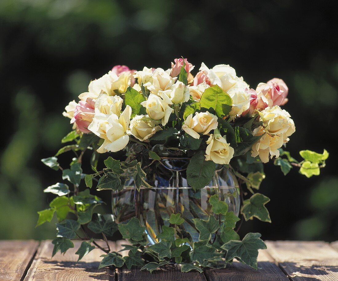 White and pastel-coloured roses with ivy in bulbous glass vase