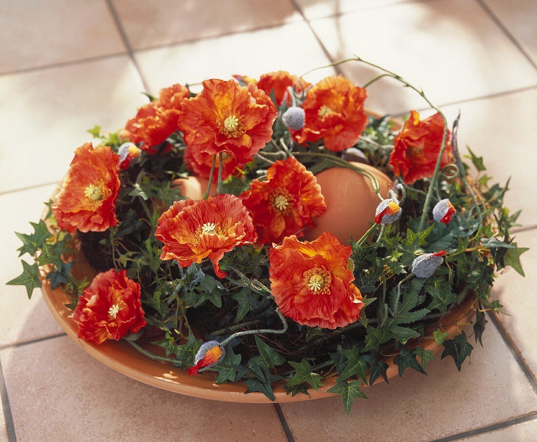 Brown eggs in terracotta bowl with artificial poppies and ivy