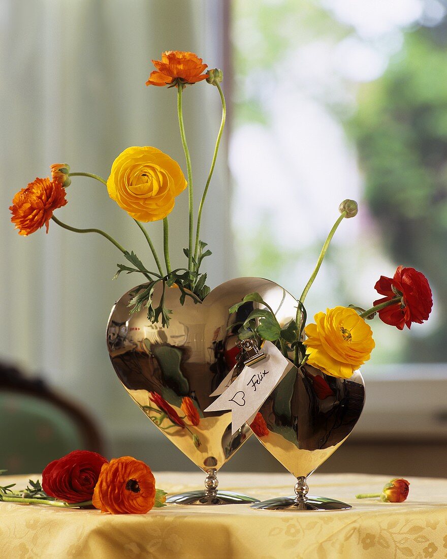 Gelbe, rote & orangene Ranunkeln in einer herzförmigen Vase