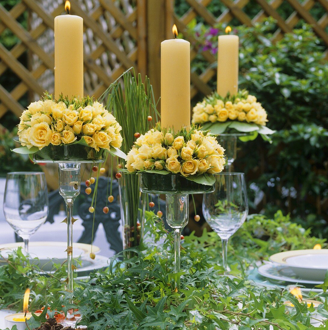 Gelbe Kerzen mit Rosen in Kerzenleuchtern aus Glas auf Tisch