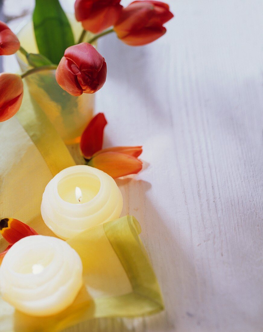 Burning candles, green fabric napkins and red tulips
