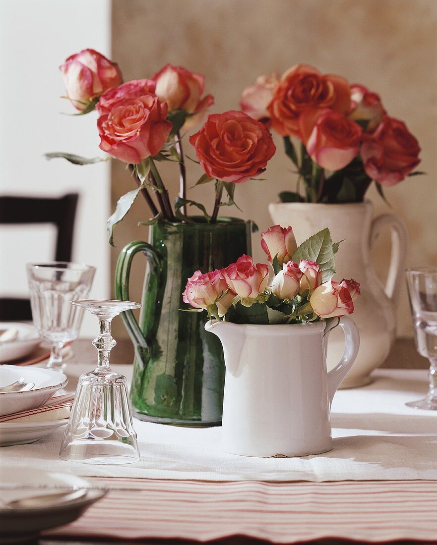 Rosen in Keramikkrügen auf gedecktem Tisch