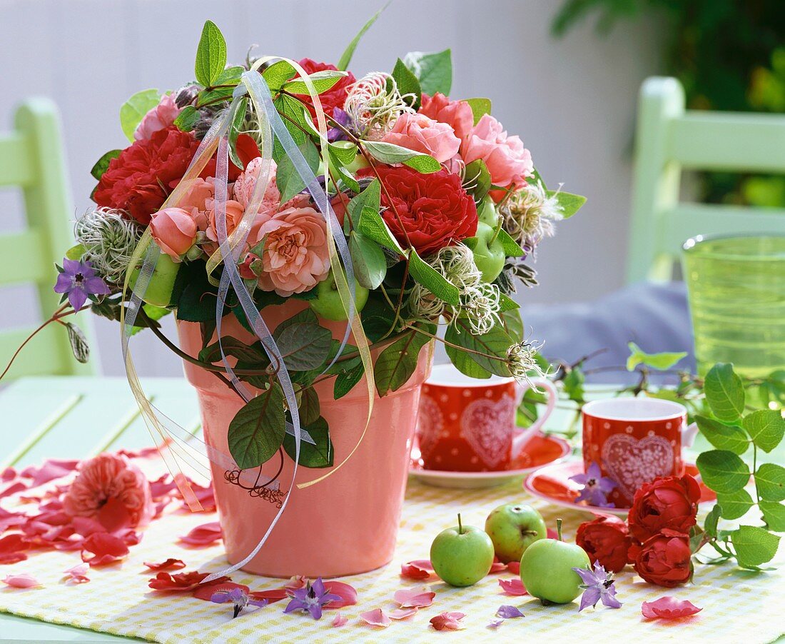 Sommerstrauss aus Rosen, Clematis und Borretsch in rosa Vase, unreife Äpfelchen als Deko