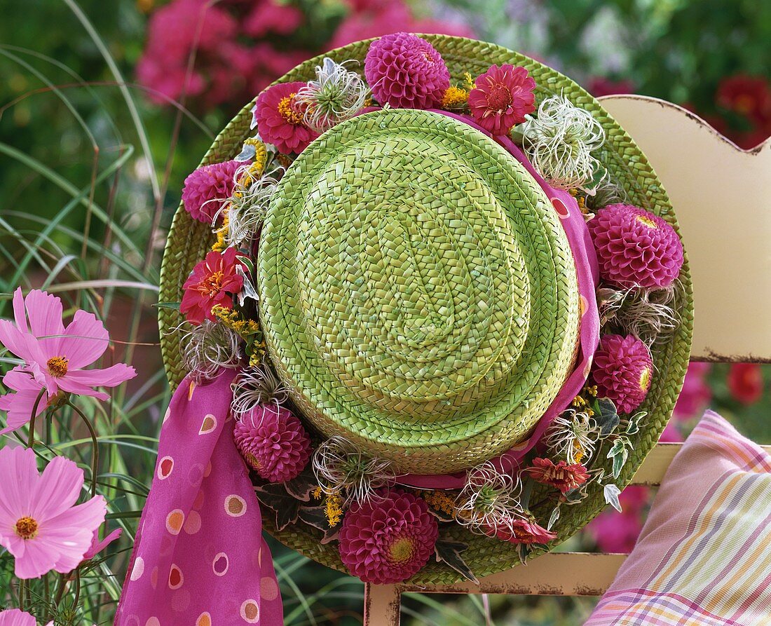 Green straw hat with wreath of dahlias on garden chair
