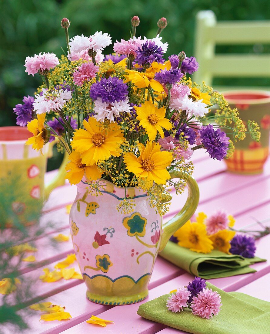 Sommerlicher Blumenstrauss mit Mädchenauge, Kornblumen und Fenchelblüten auf Gartentisch