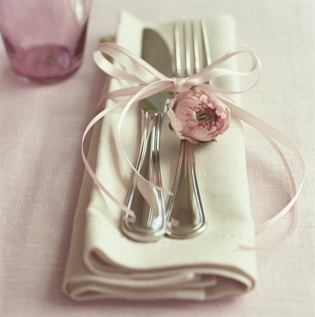 Silberbesteck mit Schleife und rosa Blüte auf Stoffserviette