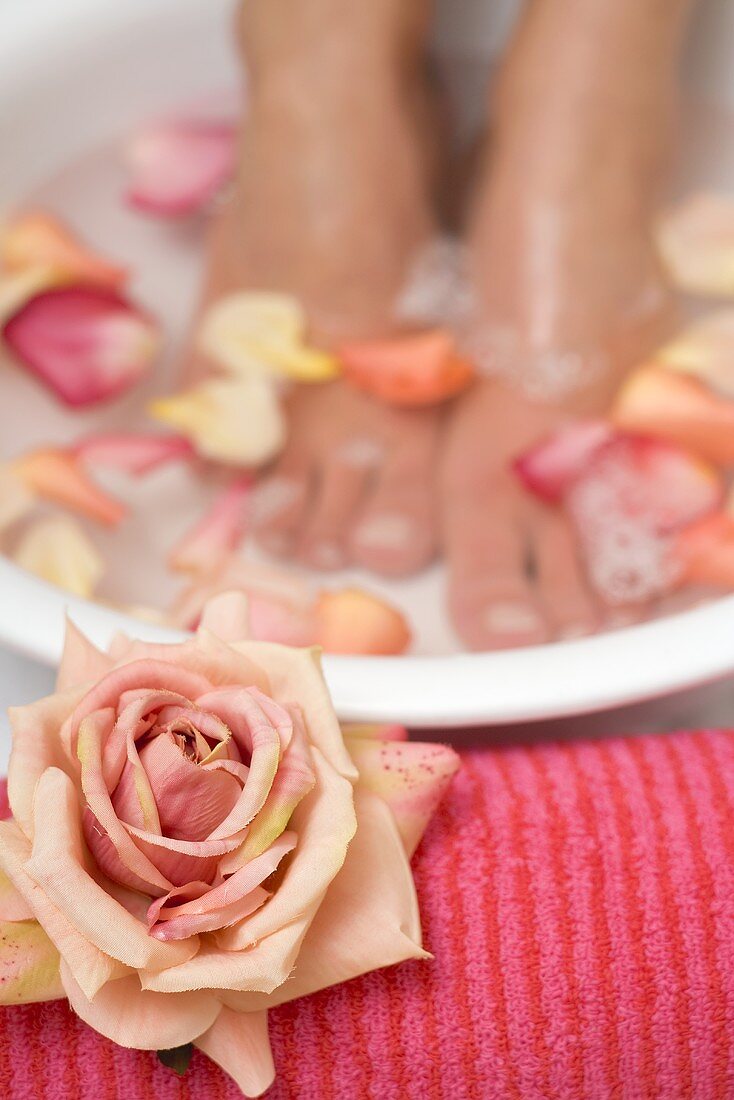 Frau nimmt wohltuendes Fussbad mit Rosenblütenblättern