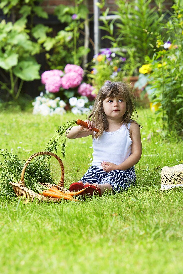 A little girl sitting on a lawn with carrots