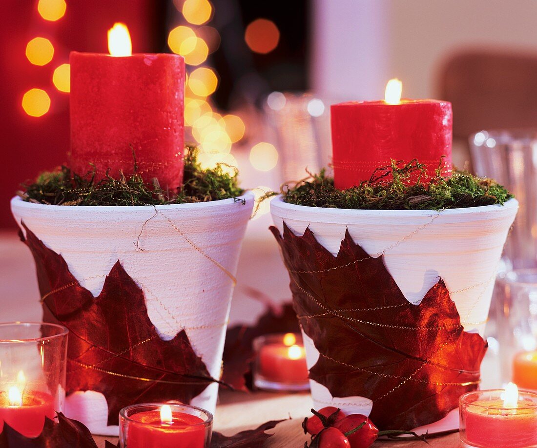 Töpfe mit Blätterdeko und roten Kerzen
