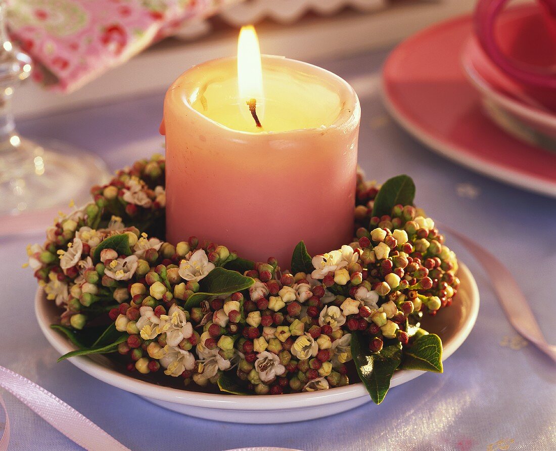 Kerze umgeben von Kranz aus Lorbeerschneeball auf Teller