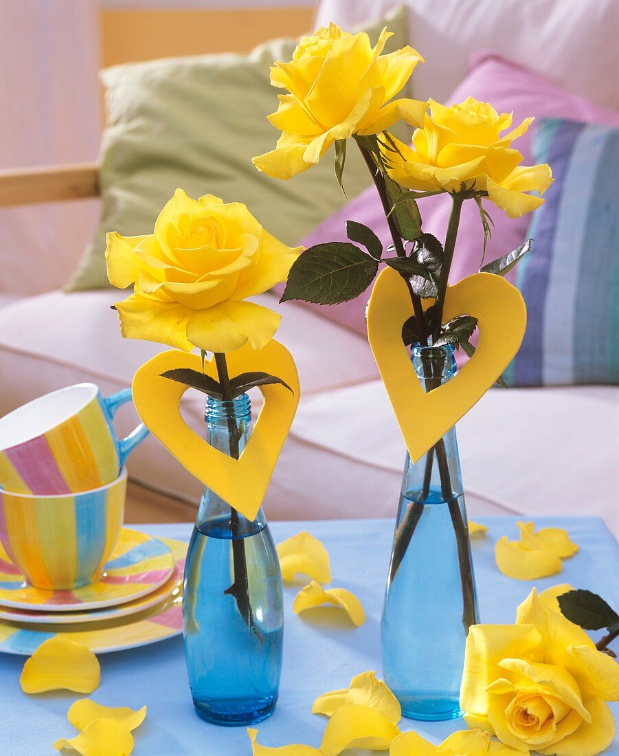 Gelbe Rosen mit Moosgummiherzen in blauen Flaschen
