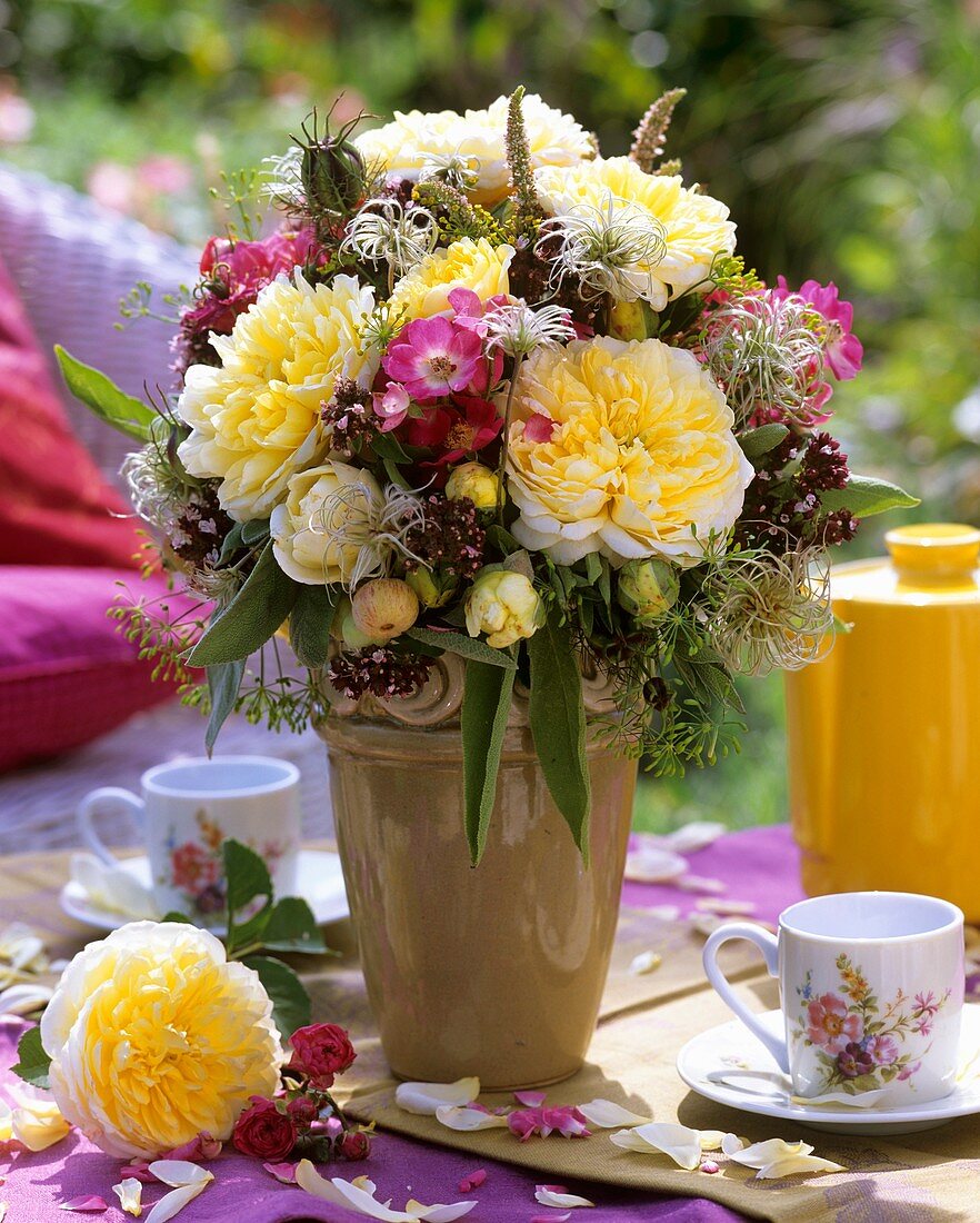 Vase of summer flowers on table laid for coffee outdoors