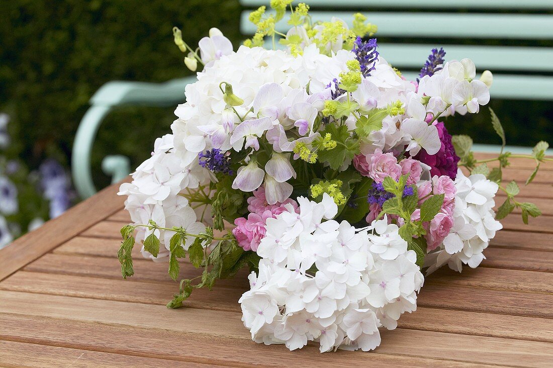 Sommerlicher Blumenstrauss mit Hortensien auf Gartentisch