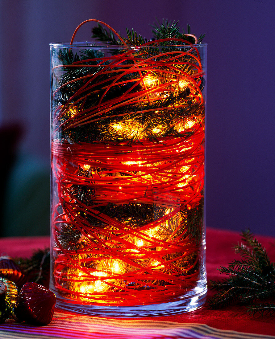 Glas mit Fichtenzweigen, Peddigrohr und Lichterkette