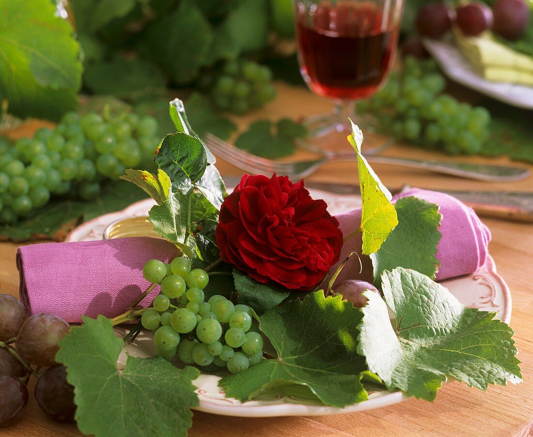 Dunkelrote Rose mit Weintrauben und -blätter als Tellerdeko