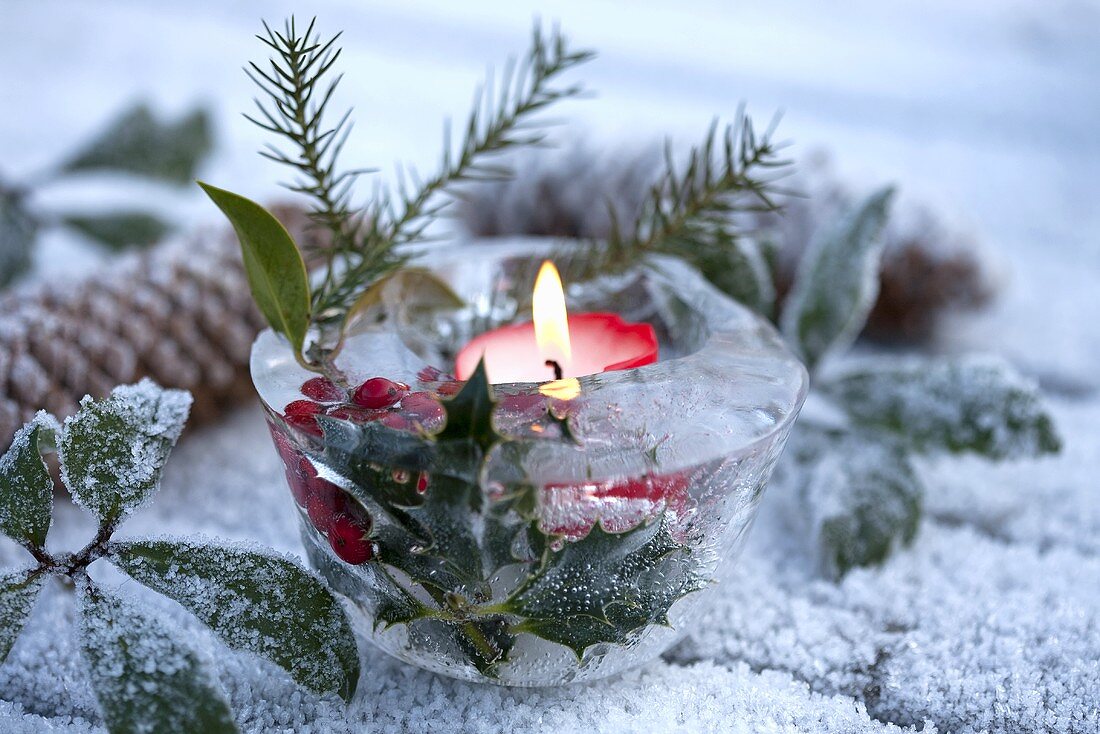 Eisschale mit Ilex und Kerze als weihnachtliche Gartendeko