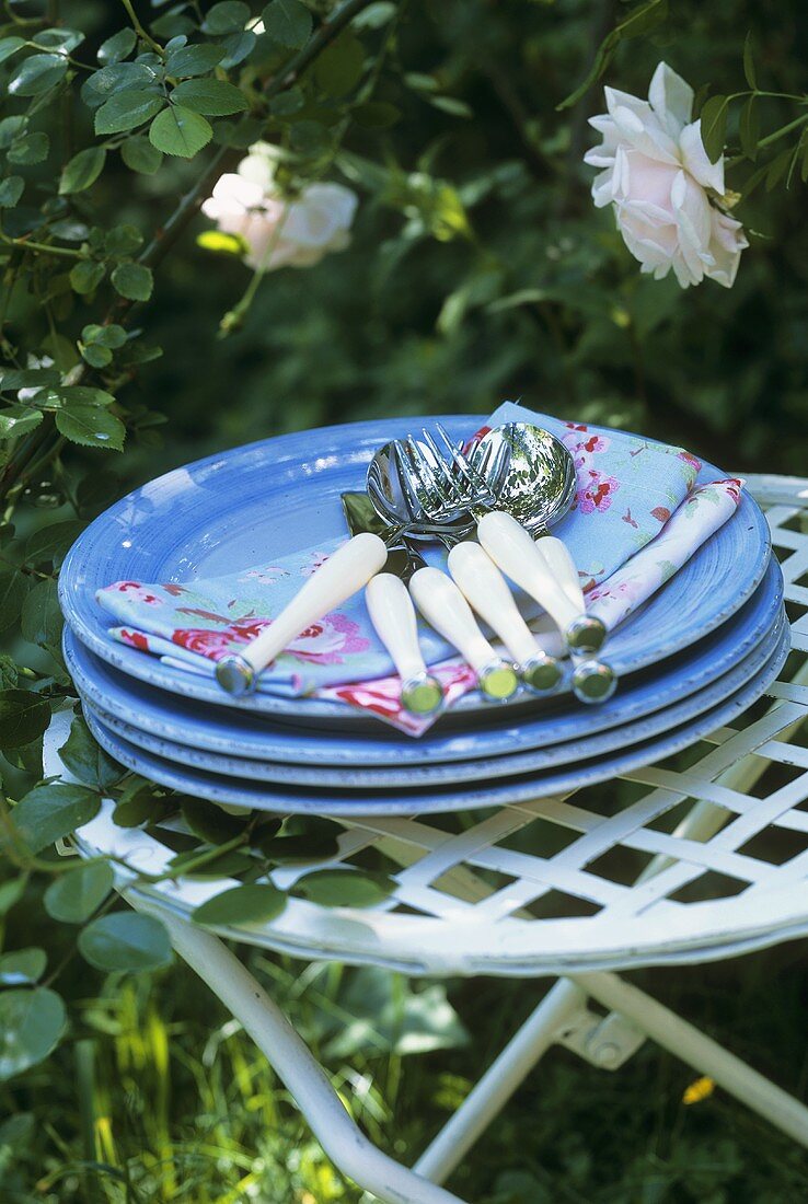 Tellerstapel mit Servietten und Besteck auf einem Gartentisch