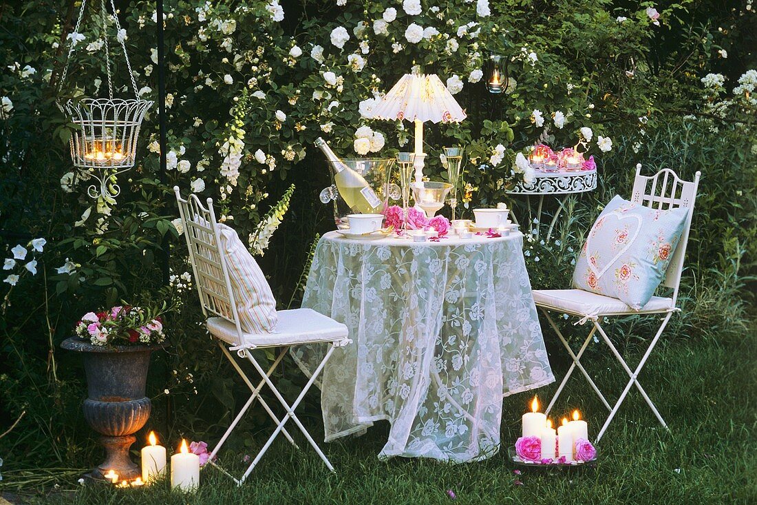 Table and chairs by candlelight in a rose garden
