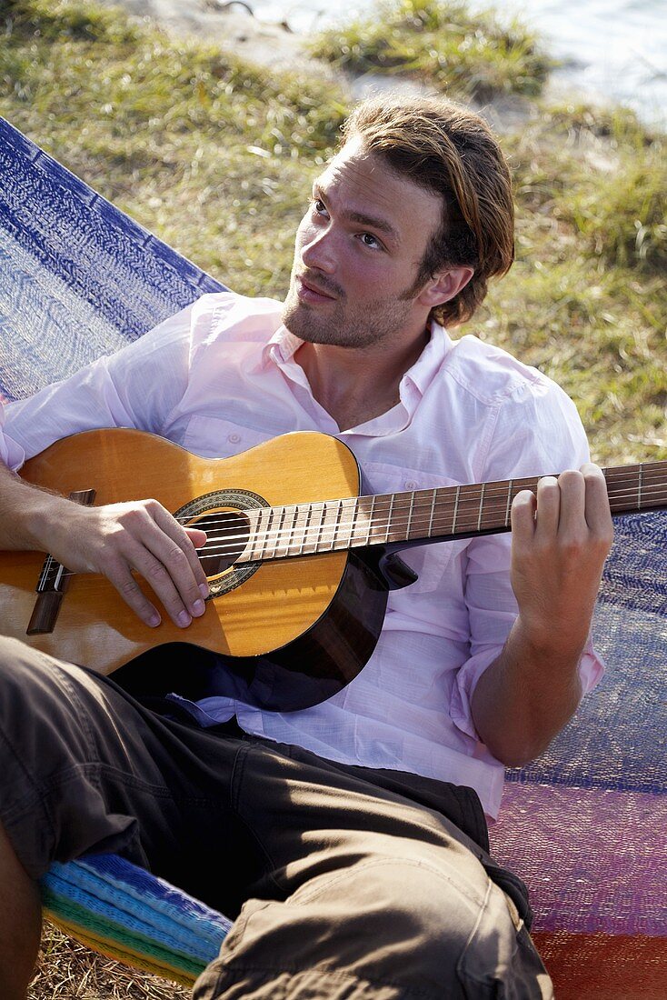 Junger Mann spielt Gitarre in einer Hängematte sitzend