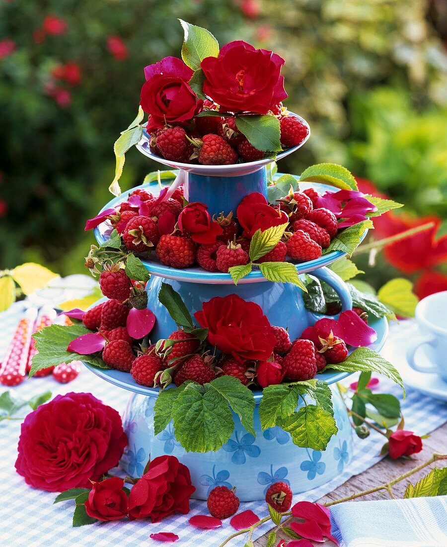 Raspberries & red roses on tiered stand of upturned cups & plates