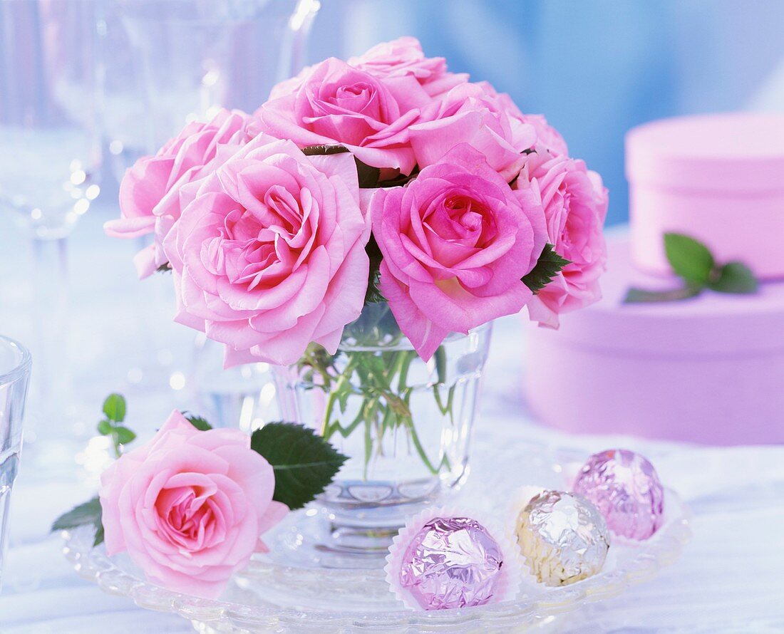 Strauss aus rosa Rosen, daneben Pralinen und Geschenkkartons