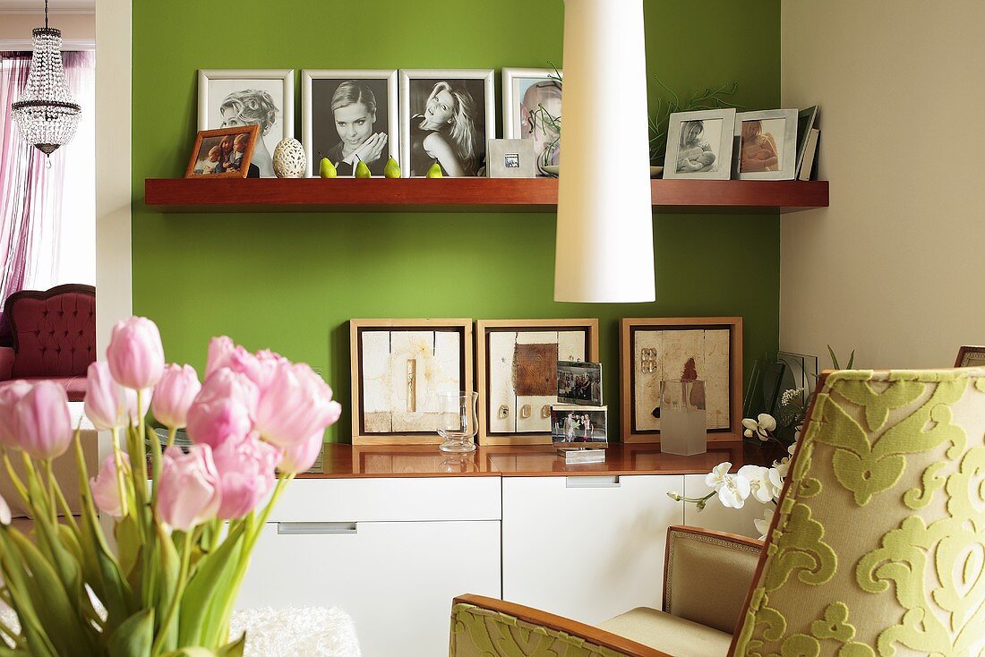 Moderne Kommode und passendes Holzregal mit Familienfotos vor grün-gestrichene Wand