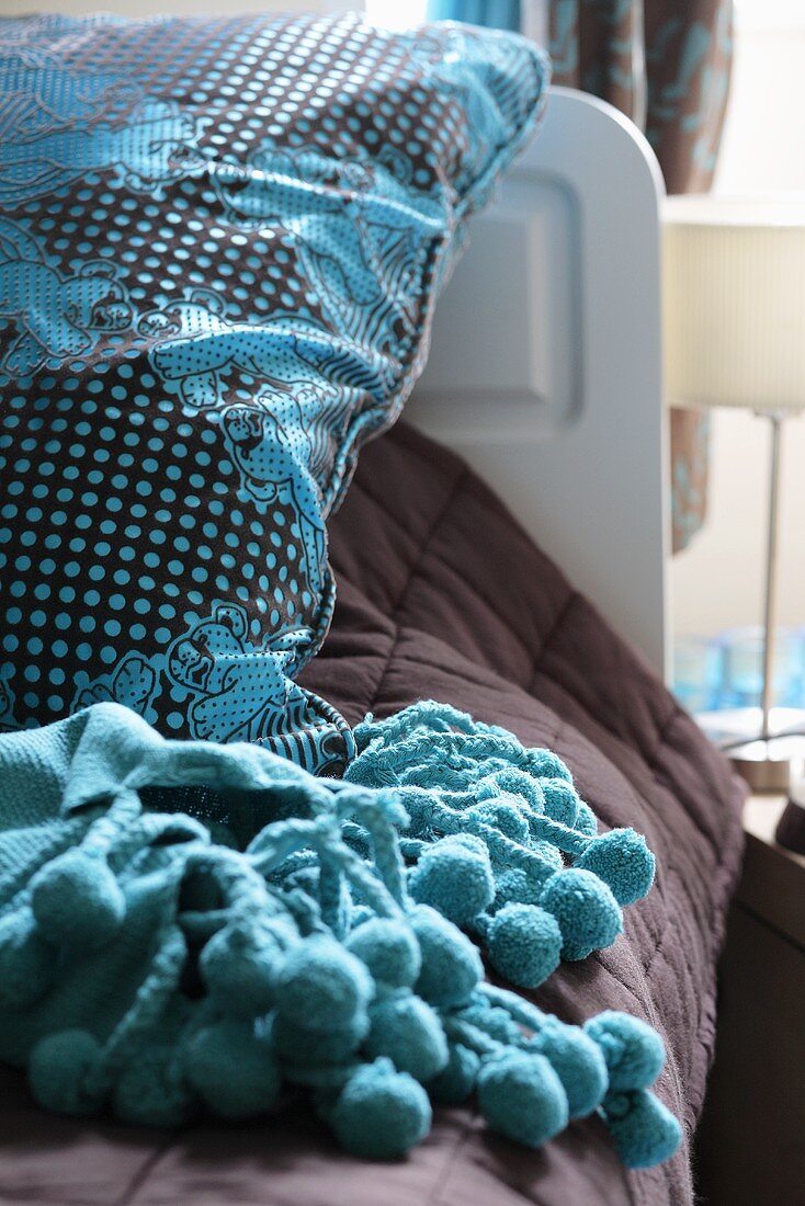 Brown and turquoise pillow and matching blanket fringed with pompoms