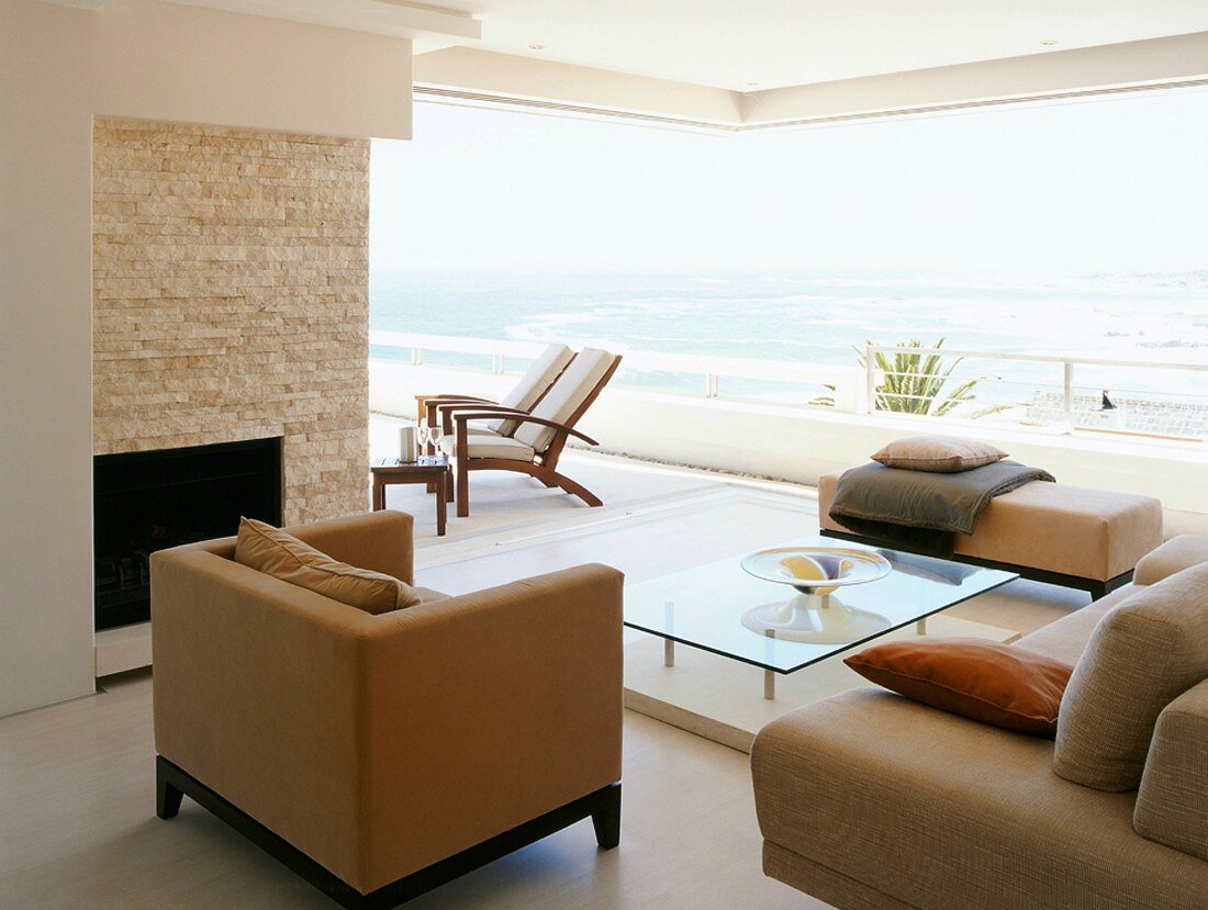 Moderne Sofagarnitur vor offener Fensterfront mit Ausblick auf Terrasse und Meer