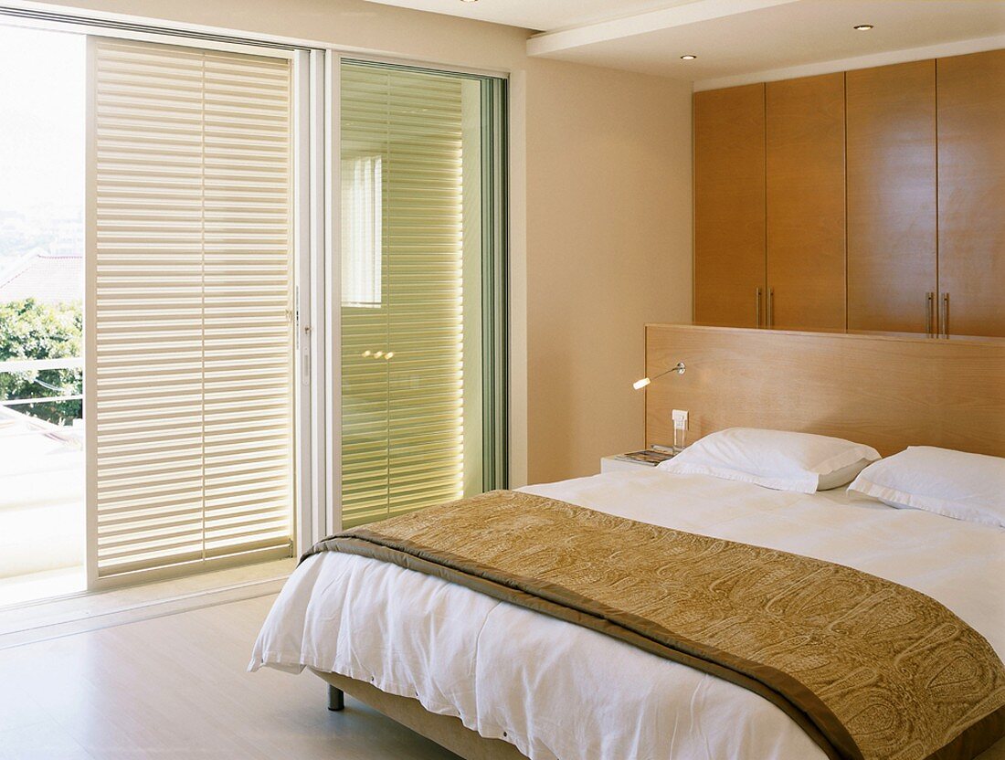 Double bed with partition headboard in modern bedroom with shutters on wide sliding windows