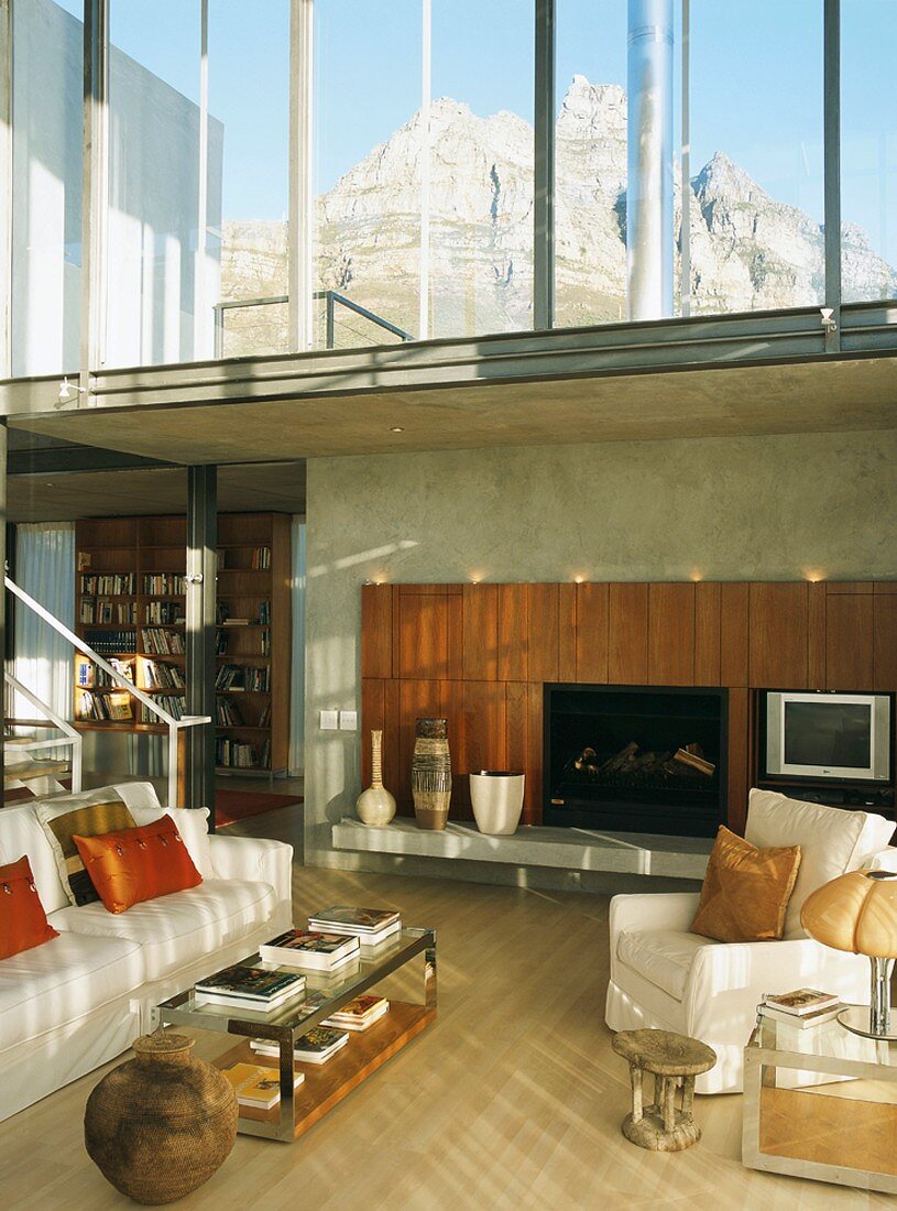 Zeitgenössische Architektur mit Sitzplatz vor Kamin in zweigeschossigem Wohnraum und Blick auf hohe Berge