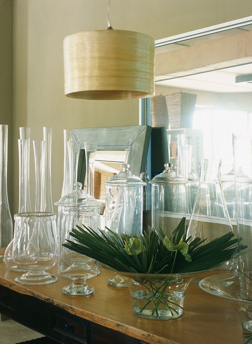 Various, empty glass vessels and arrangement of leaves in bowl next to mirrored top of dresser