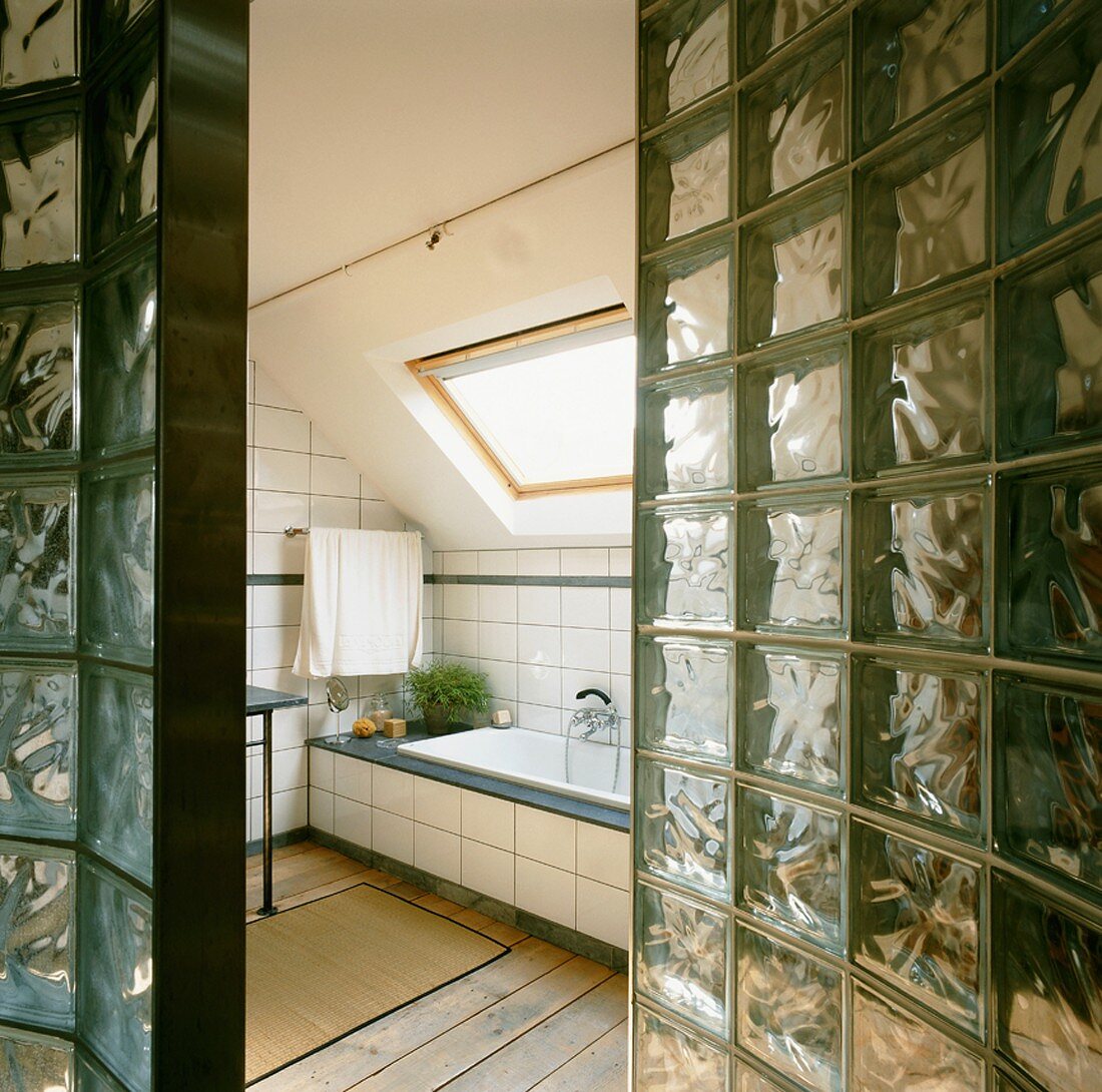 Blick durch Wand aus Glasbausteinen in Bad ensuite mit Dachflächenfenster über der eingebauten Wanne