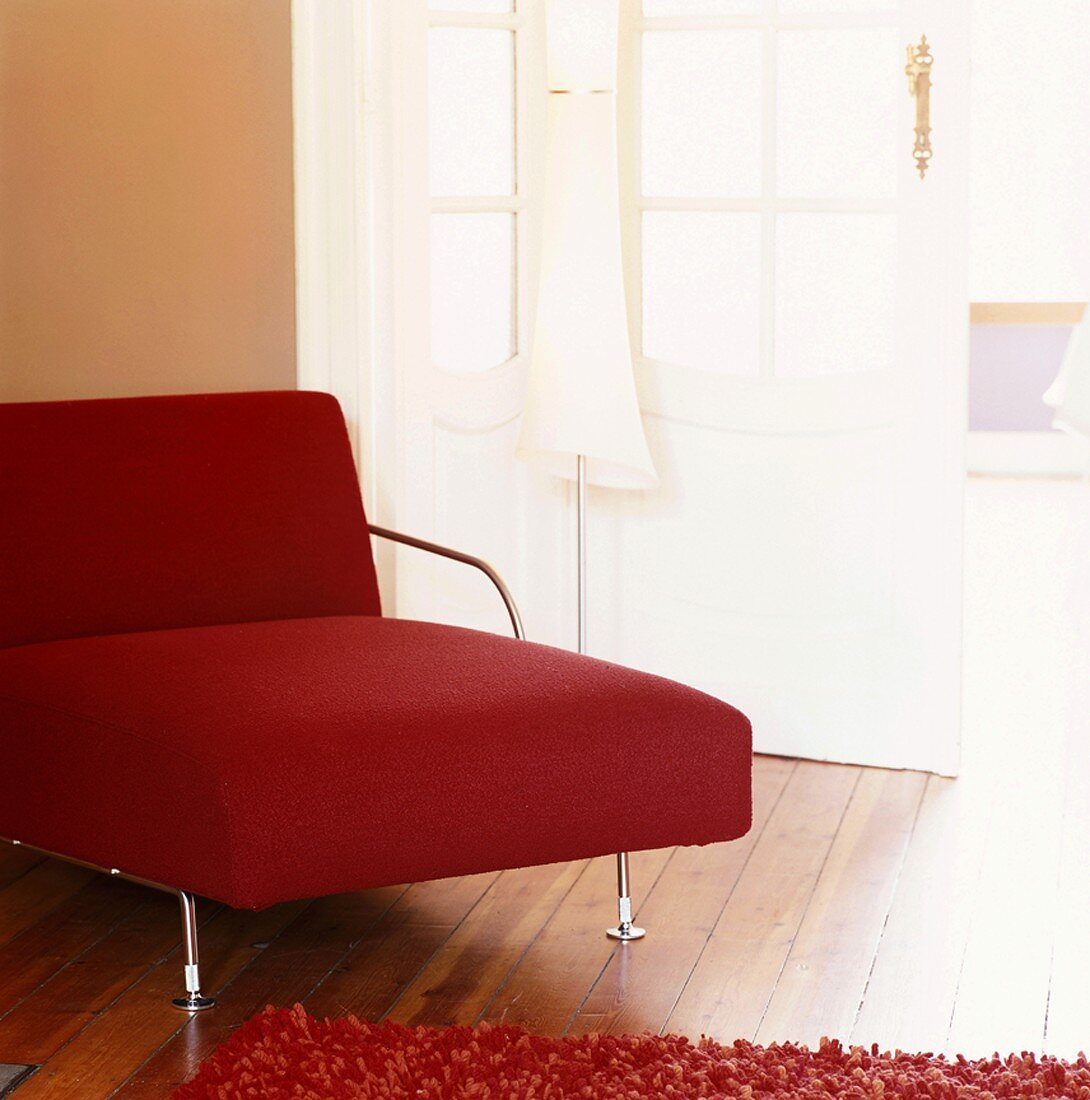 Rote Chaise longue mit zierlichem Stahlgestell und Stehlampe vor weisser Altbautür