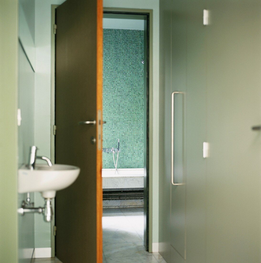 Blick vom Vorraum mit Handwaschbecken in das türkis geflieste Badezimmer