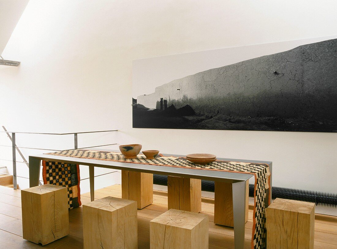 Im Ethnostil dekorierter, minimalistischer Esstisch aus Metall mit kubischen Baumstammhockern