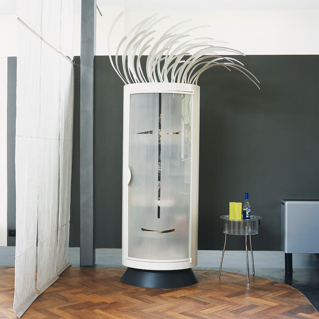 Runder Designer-Schrank mit stilisiertem Gesicht in der Milchglastür und Punkfrisur in Wohnraum mit Loftcharakter